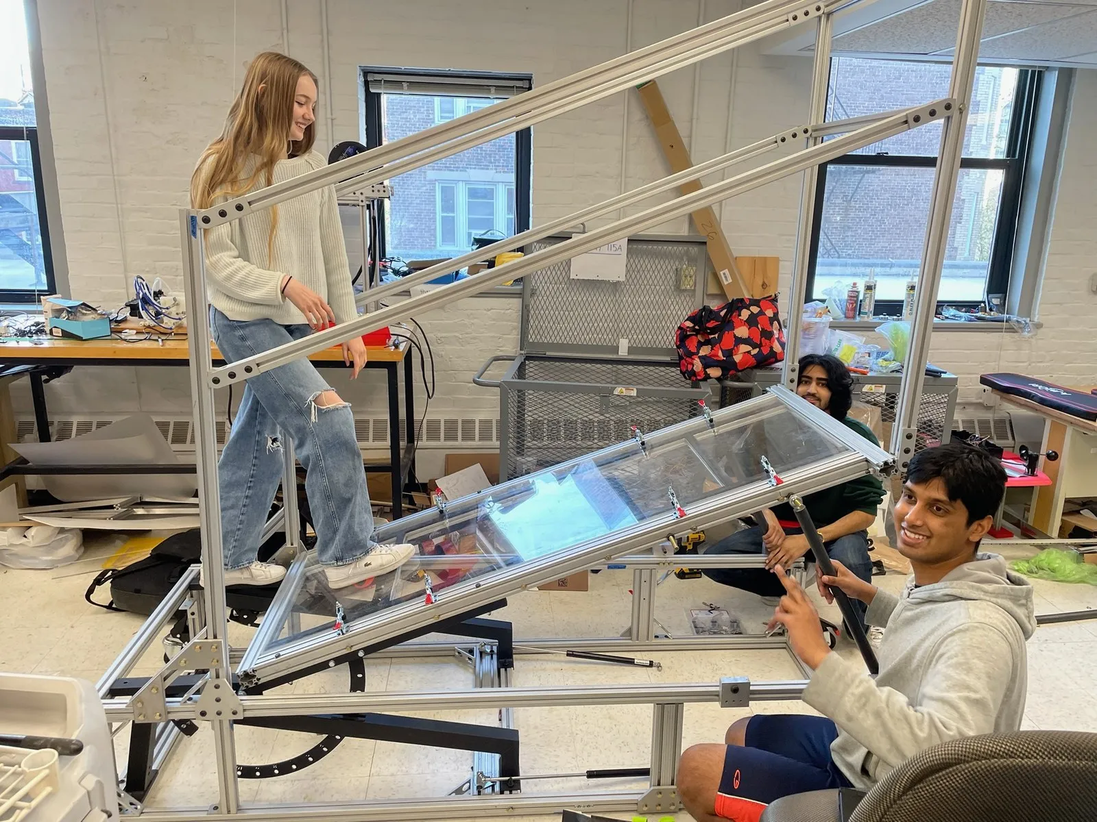 A teammate walks down the inclined clear acrylic walkway while two teammates watch in the makerspace.