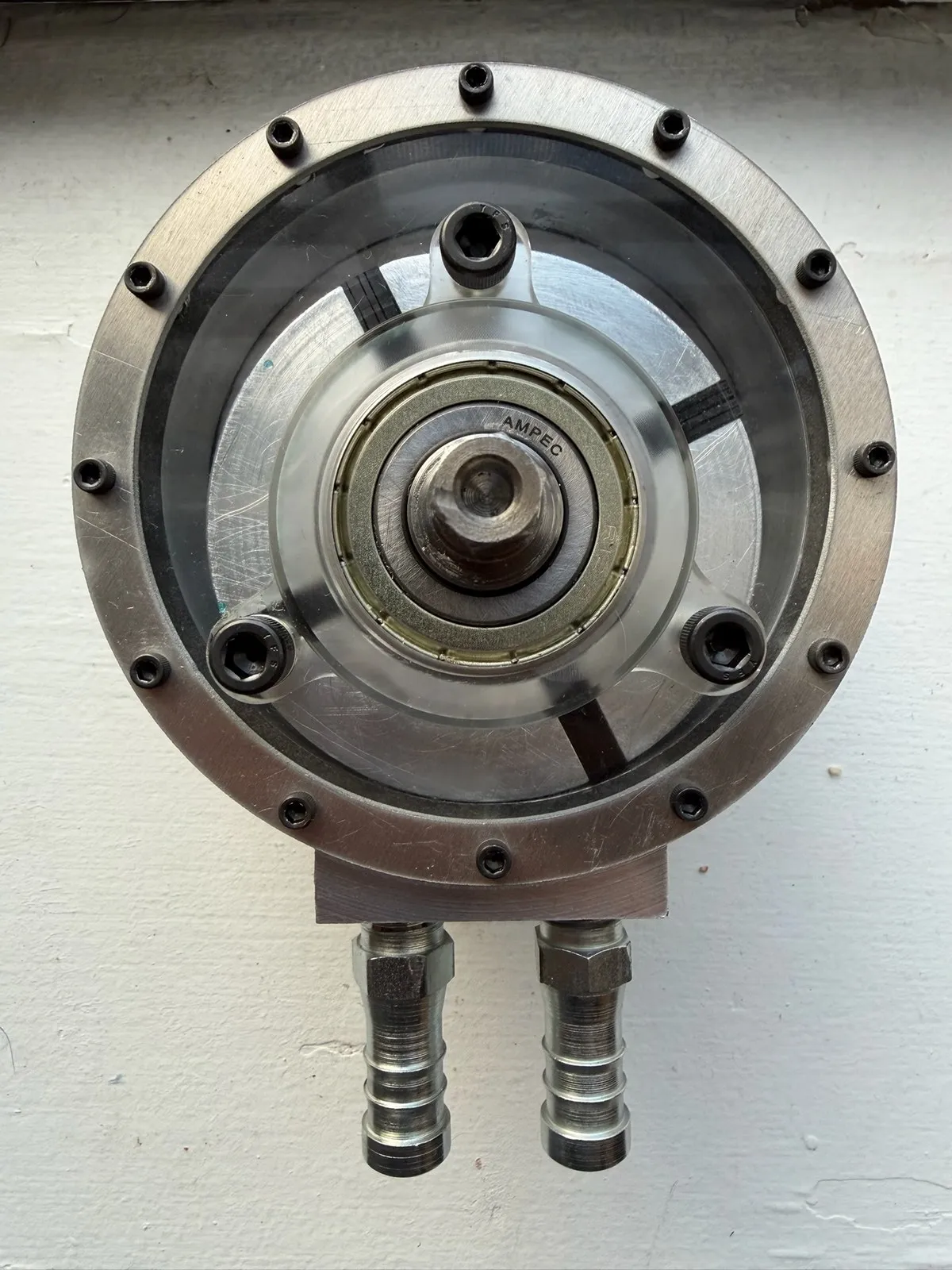 Machined aluminum vane pump head-on: clear front plate, slotted rotor and vanes, center bearing, two barbed fittings below.
